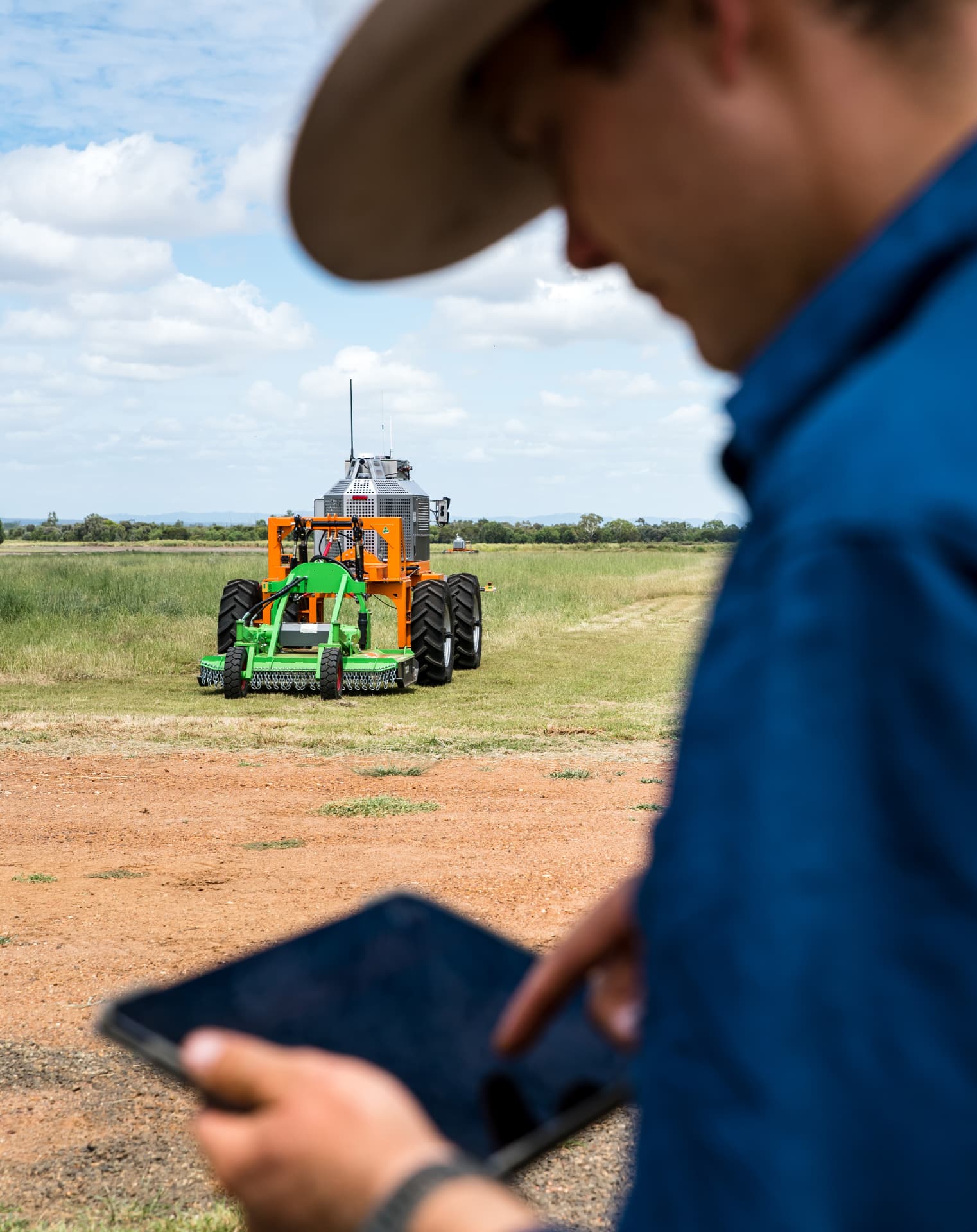 Farmer monitoring an autonomous SwarmBot mower from a tablet in the paddock